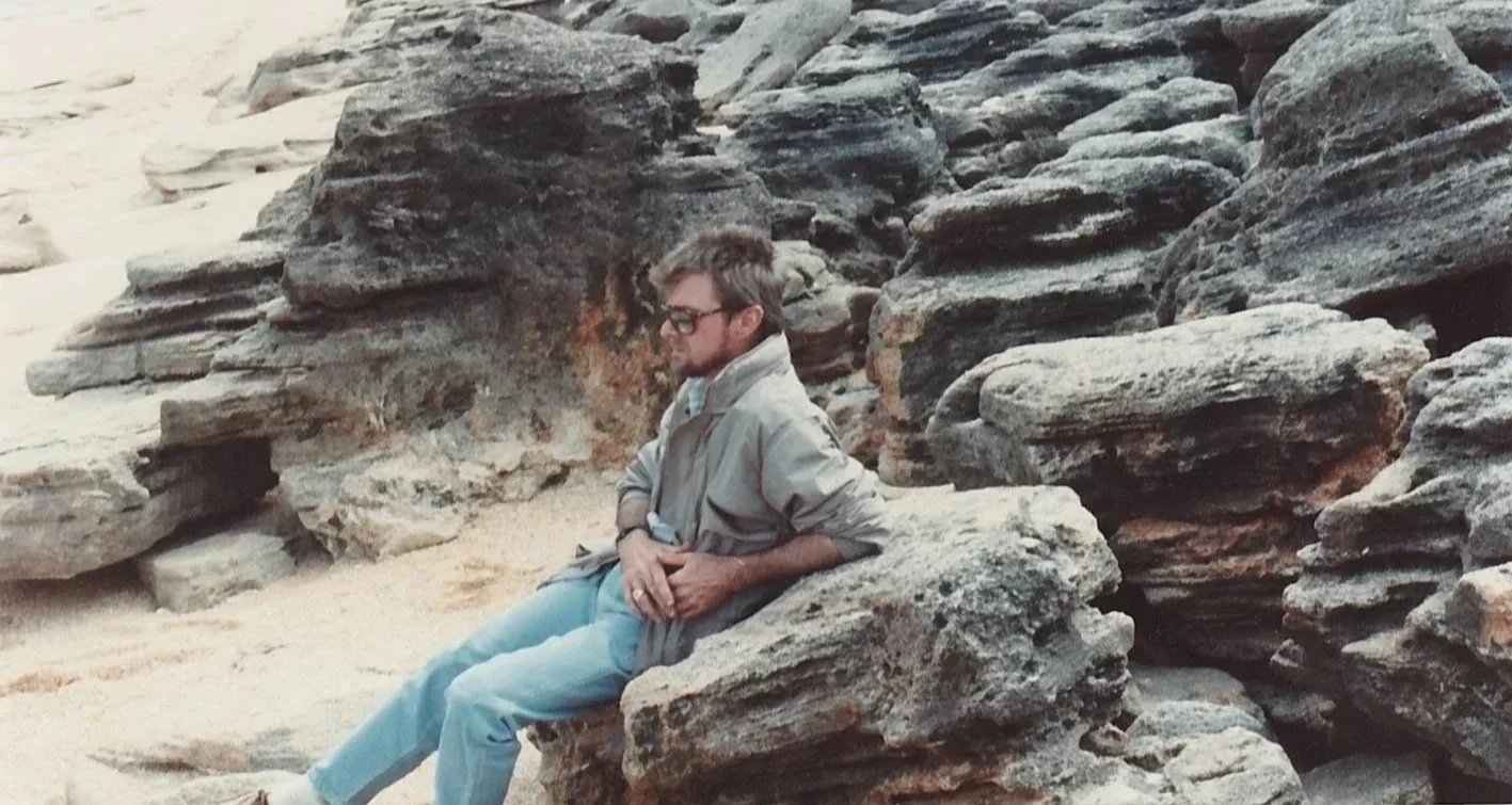 Whitney Wolf II wearing sunglasses, jeans and a bomber jacket. He is leaning against a rock at his favorite beach in Florida. Circa 1980s