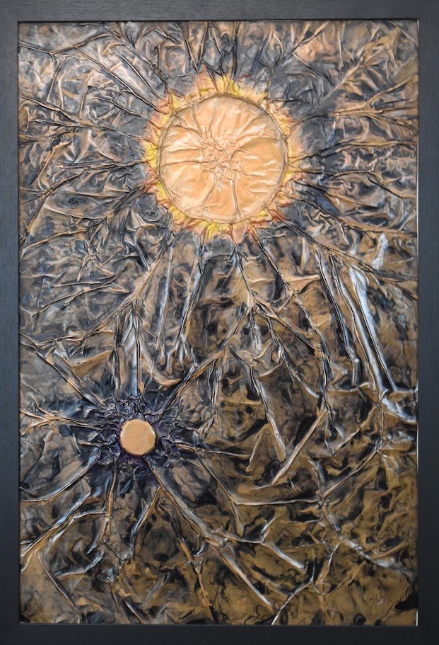 Two golden orbs radiate within a fractured metallic field. Shown close up in a black frame.