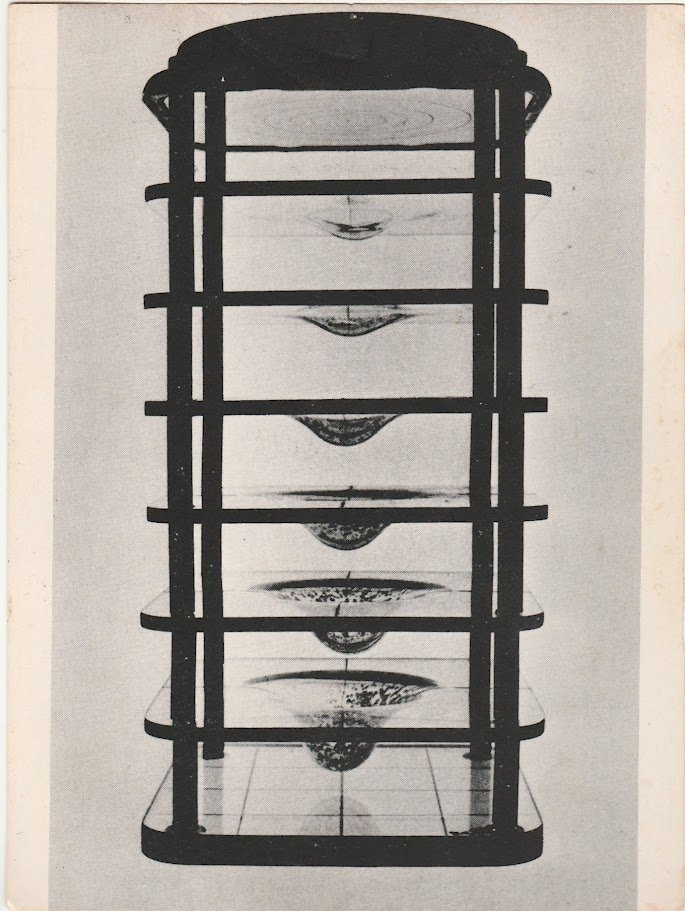 Tall black geometric structure composed of stacked horizontal shelves enclosing suspended curved forms.