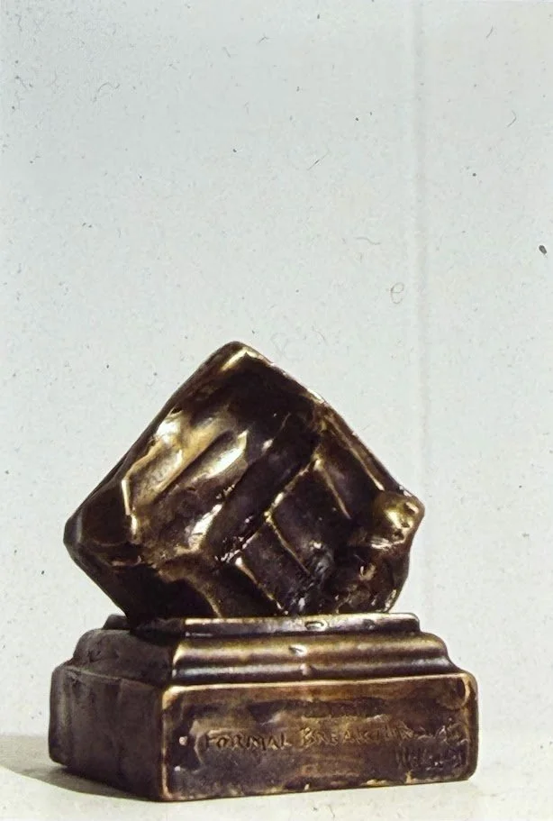 Small bronze relief mounted on a square base, featuring folded and layered forms that resemble draped fabric or carved stone.