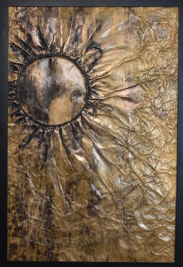A dark orb radiates through a textured field of gold and bronze. Shown close up in a black frame.