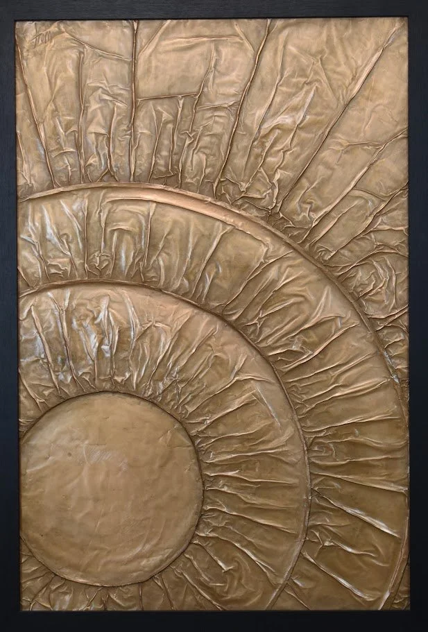 Concentric golden forms radiate outward like waves of energy. Shown close up in a black frame.