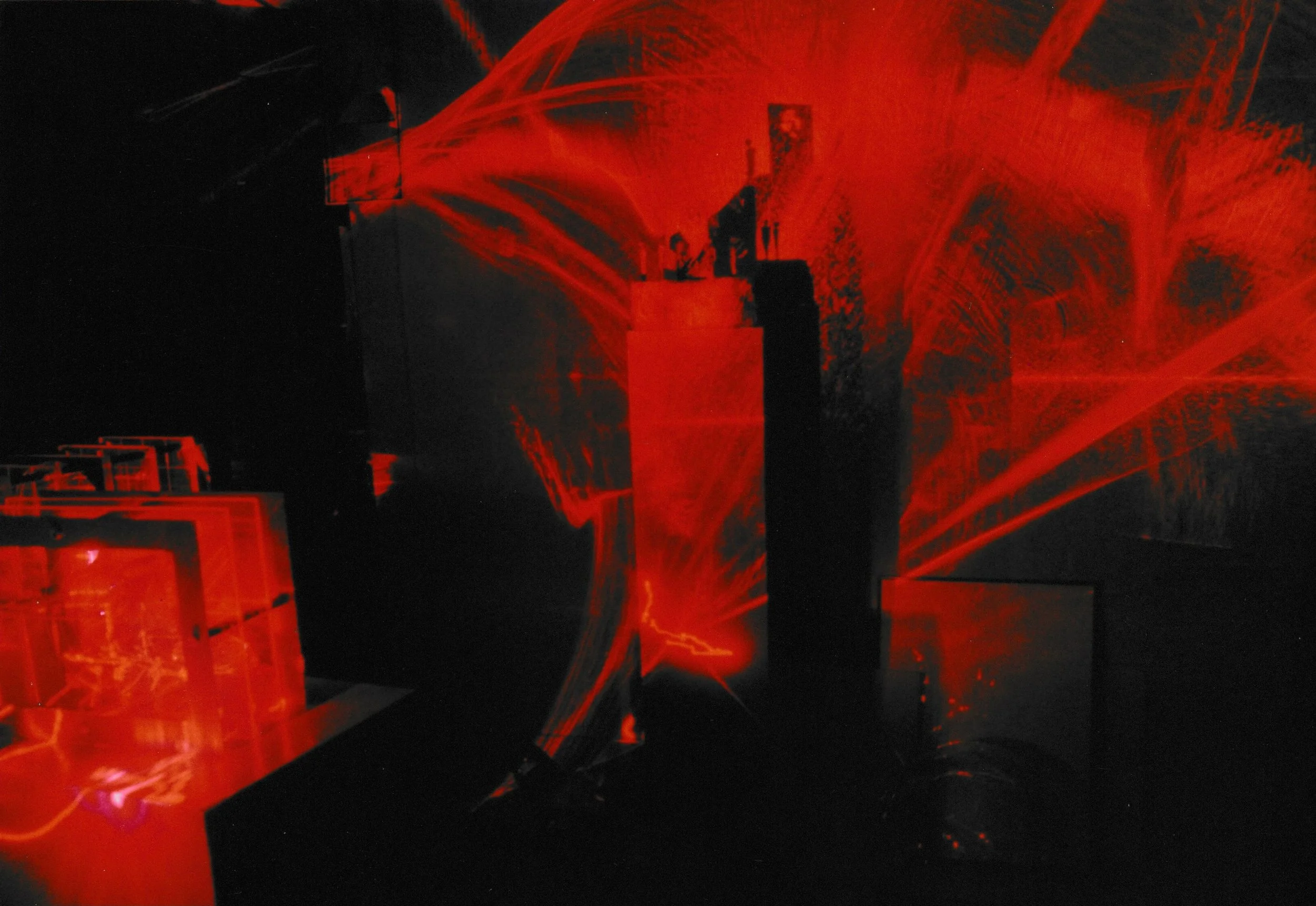 Red laser beams intersect throughout a dim exhibition space, illuminating geometric structures and suspended forms.