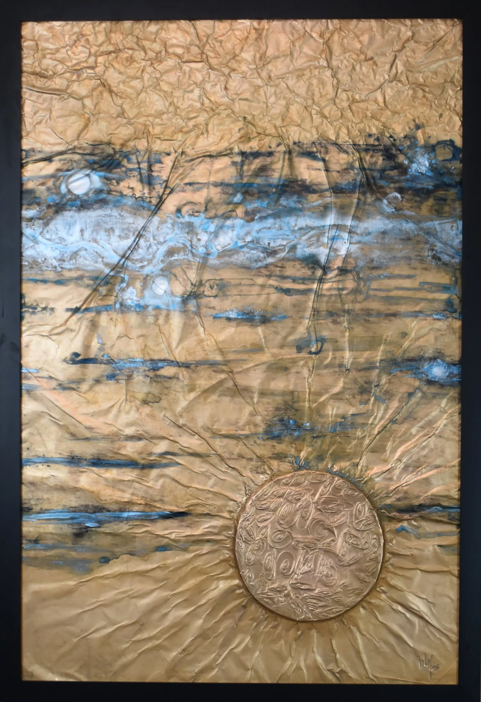 Textured gold-toned abstract artwork with blue and black horizontal markings and a raised circular form radiating outward near the bottom. Shown close up in a black frame.