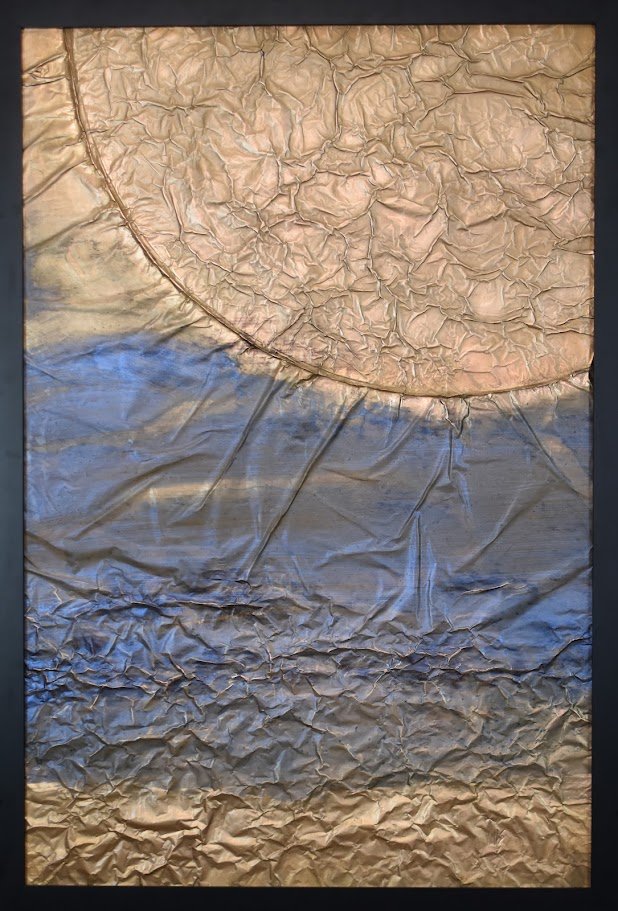 A massive golden form curves into view above layers of deep blue and metallic earth tones. Shown close up in a black frame.
