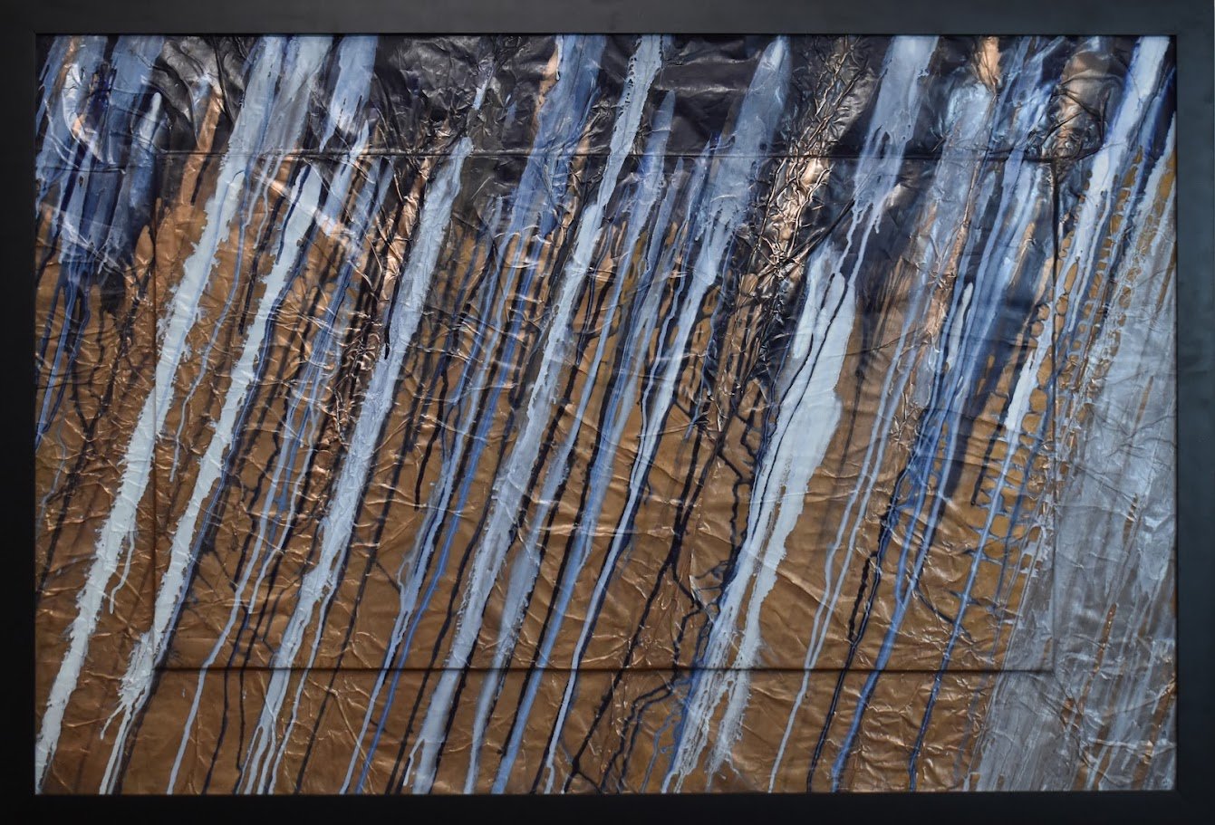Diagonal blue, white, and black streaks sweep across a textured bronze field. Shown up close in a black frame.