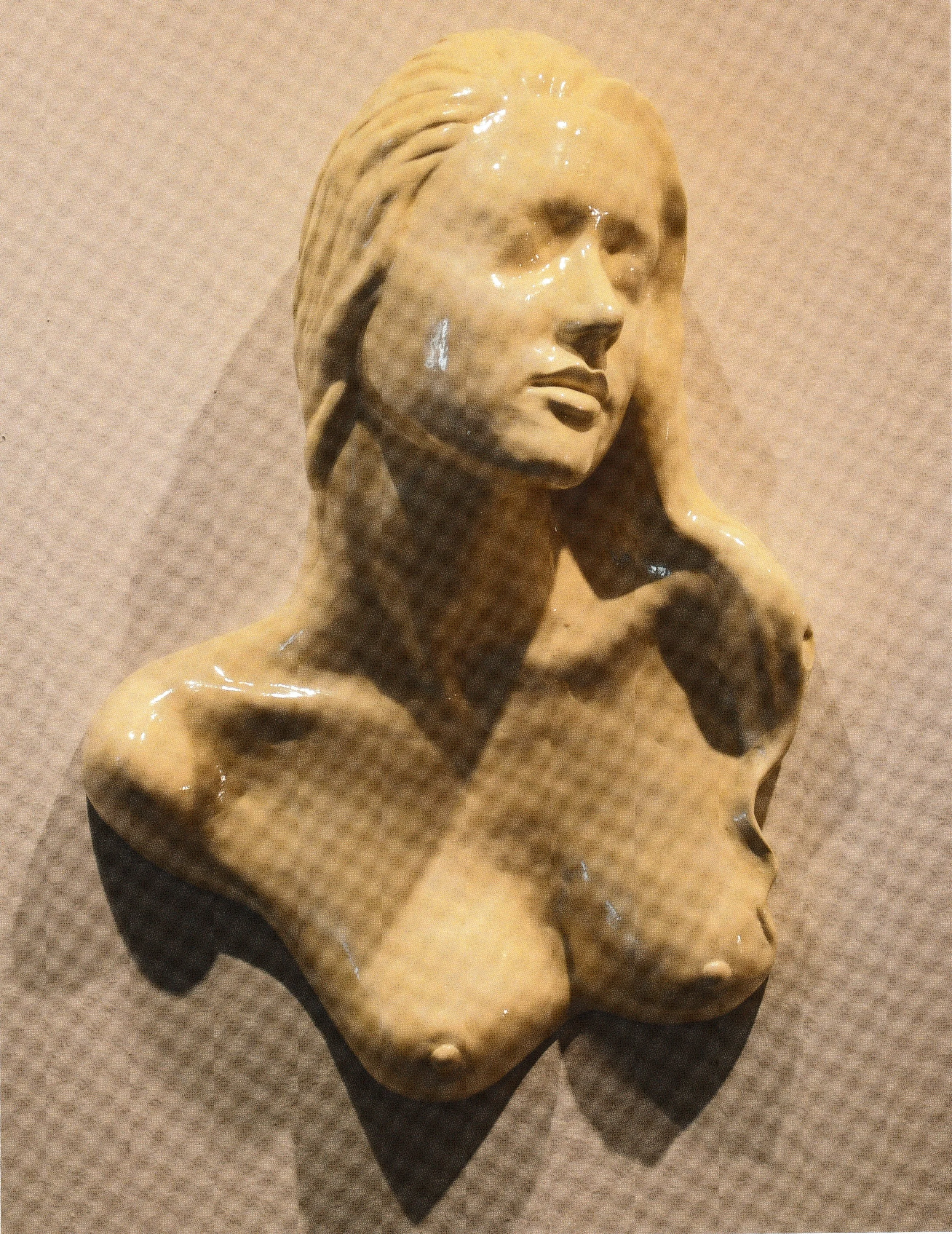 Ceramic female torso and life cast bust mounted on the wall, with exposed shoulders and face lifted upward in a tranquil gesture.