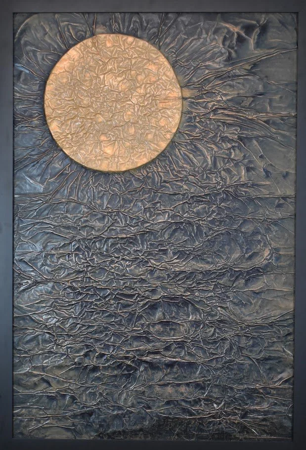 A warm, glowing orb hangs against a dark, heavily textured expanse. Shown close up in a black frame.