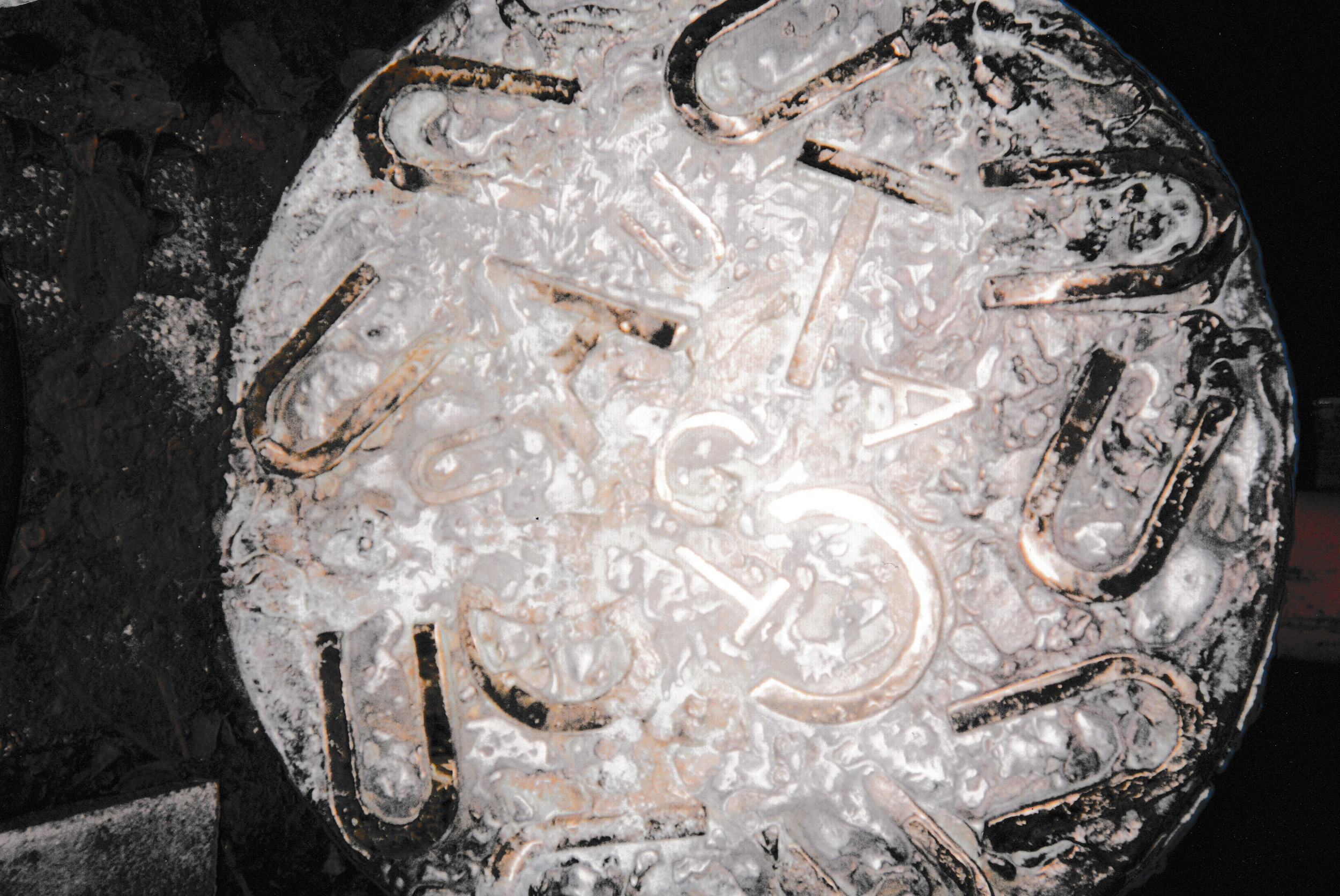 Round relief panel covered with raised letters, symbols, and abstract textures.