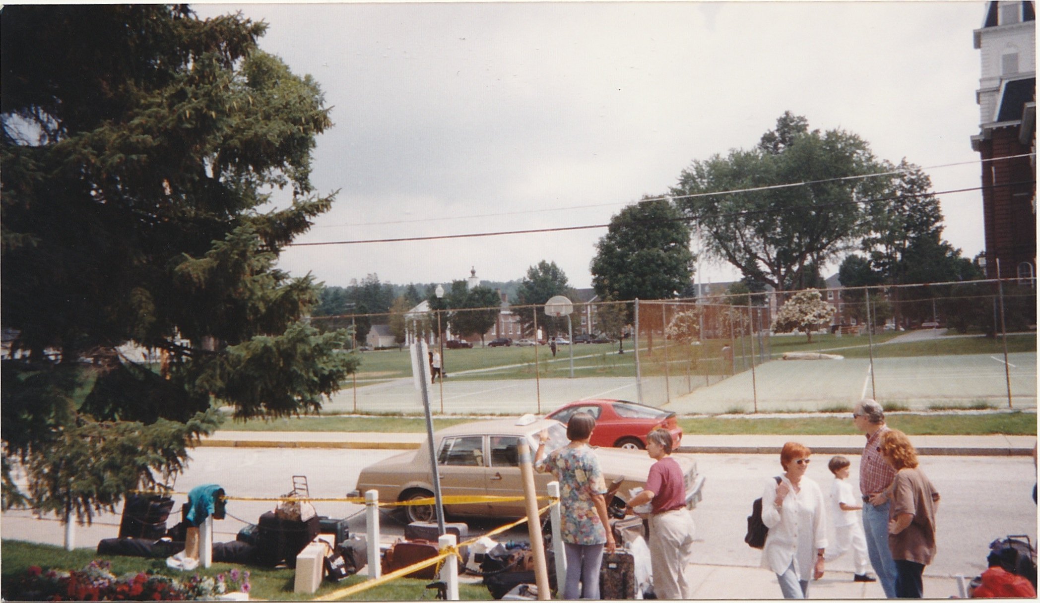 Outdoor market scene with people browsing tables and displays near a neighborhood park.