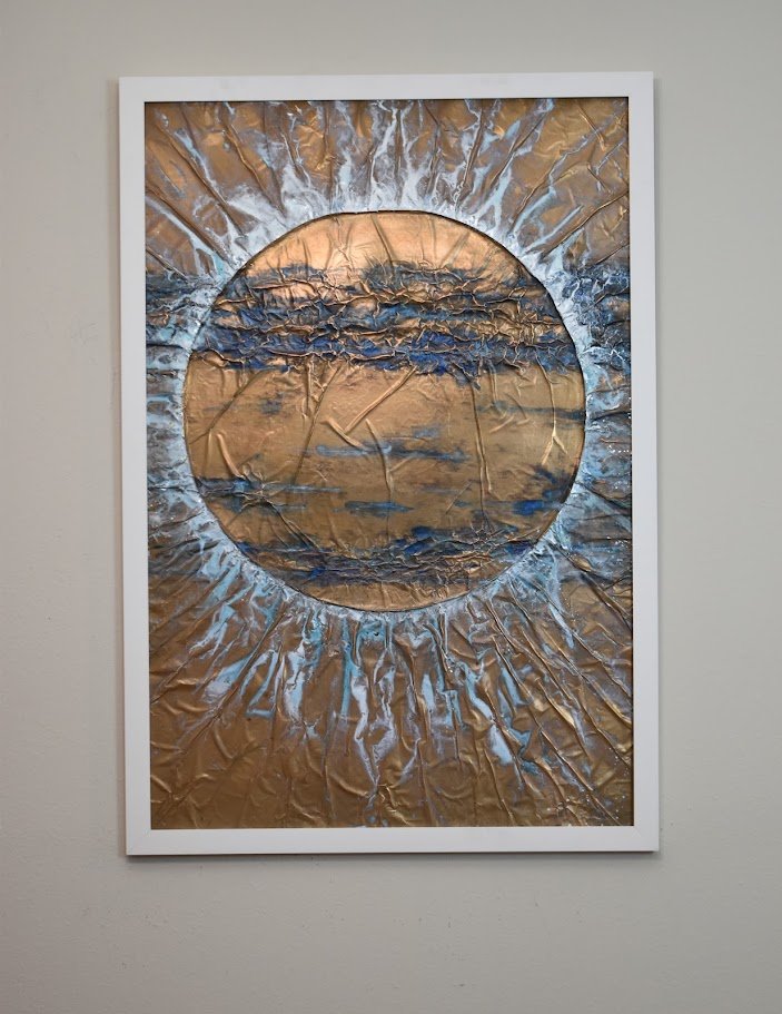 A golden orb radiates through currents of blue and silver. Displayed framed on a white wall.