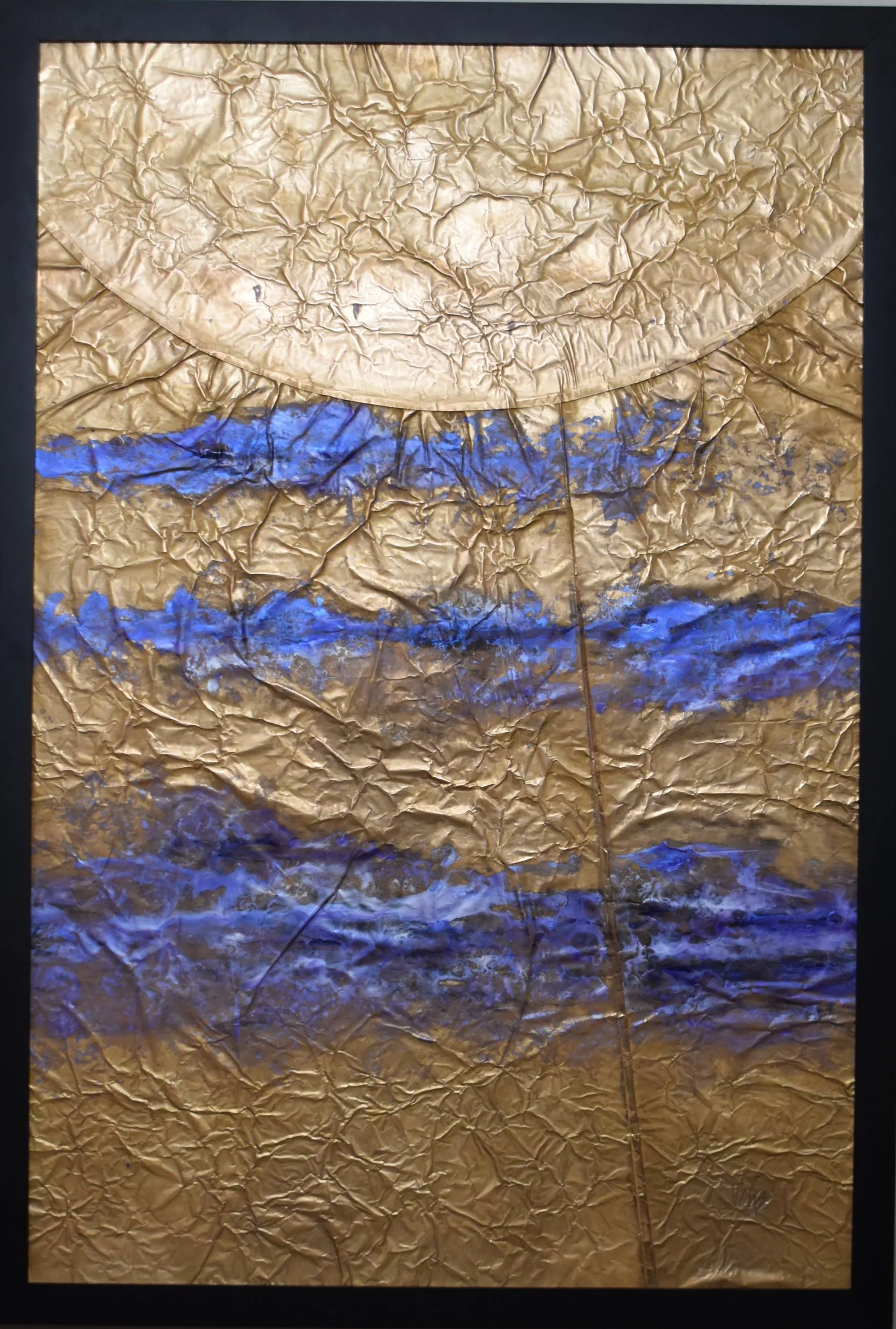 Textured gold-toned abstract artwork with horizontal bands of vivid blue and a large curved circular form extending across the top. Shown close up in a black frame.