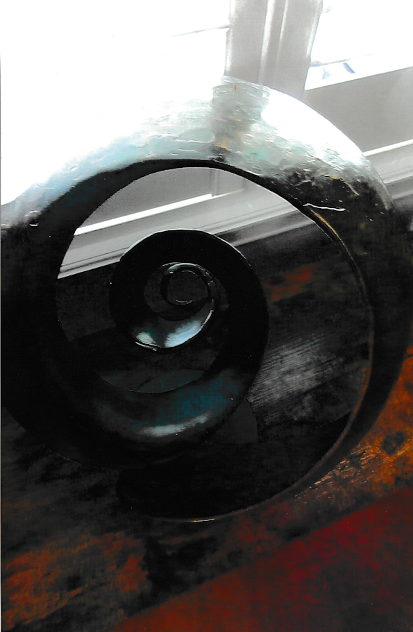 Close-up detail of a dark spiral sculpture showing concentric circular openings receding inward, emphasizing depth, curvature, and shadow.