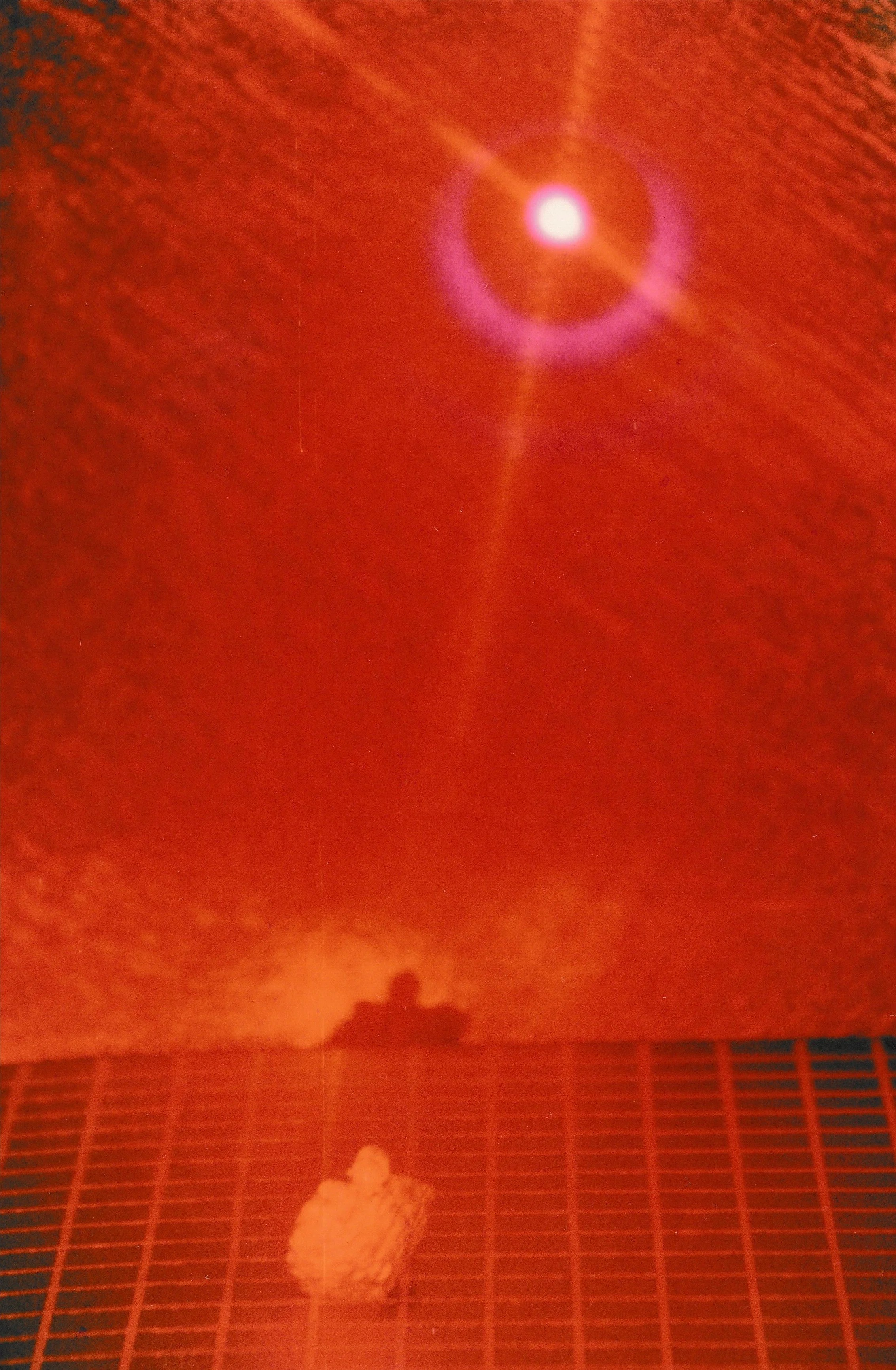 Bright red laser point suspended above a gridded surface, casting circular halos and light rays through a darkened environment.