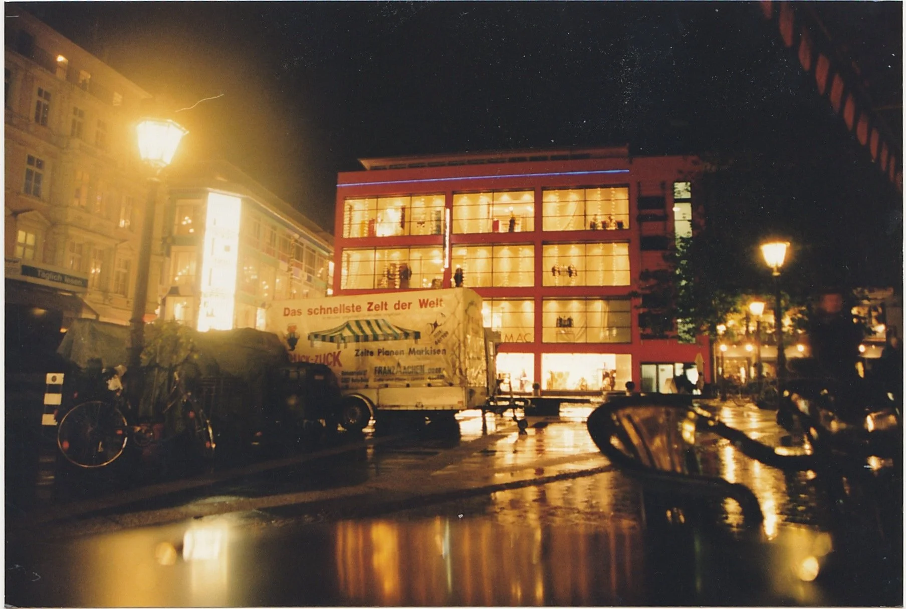 Nighttime city scene reflecting colorful lights across wet pavement.