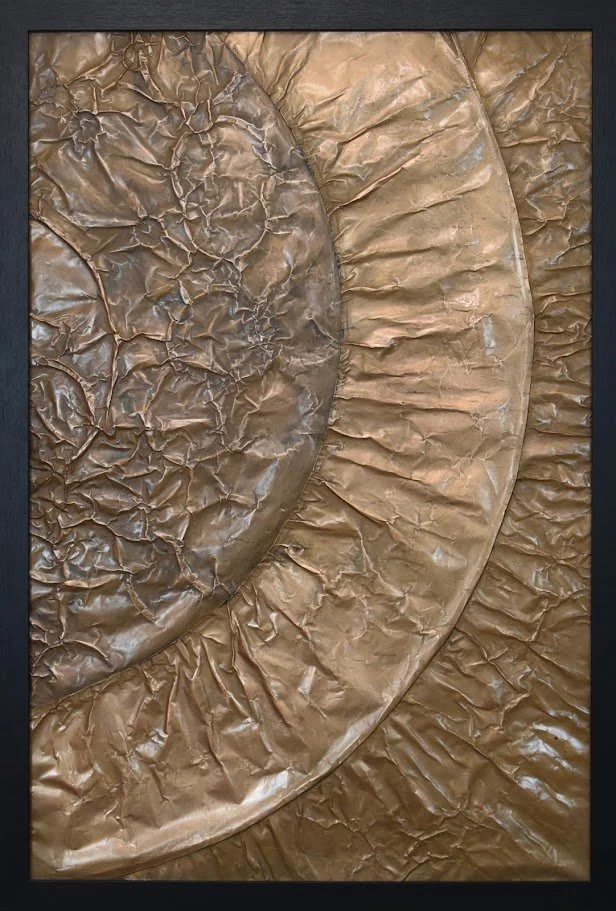 Concentric golden arcs radiate across a textured metallic field. Shown close up in a black frame.