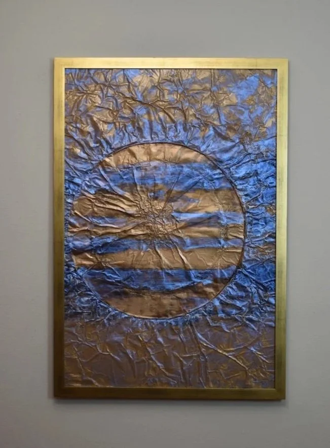 DA luminous copper-toned sphere emerges through layers of deep blue and violet, resembling a distant planet suspended in a turbulent field of space and energy. Displayed framed on a white wall.
