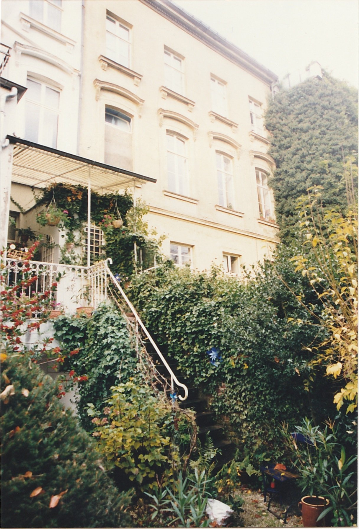 Garden pathway leading toward a house partially hidden by trees and flowering plants.