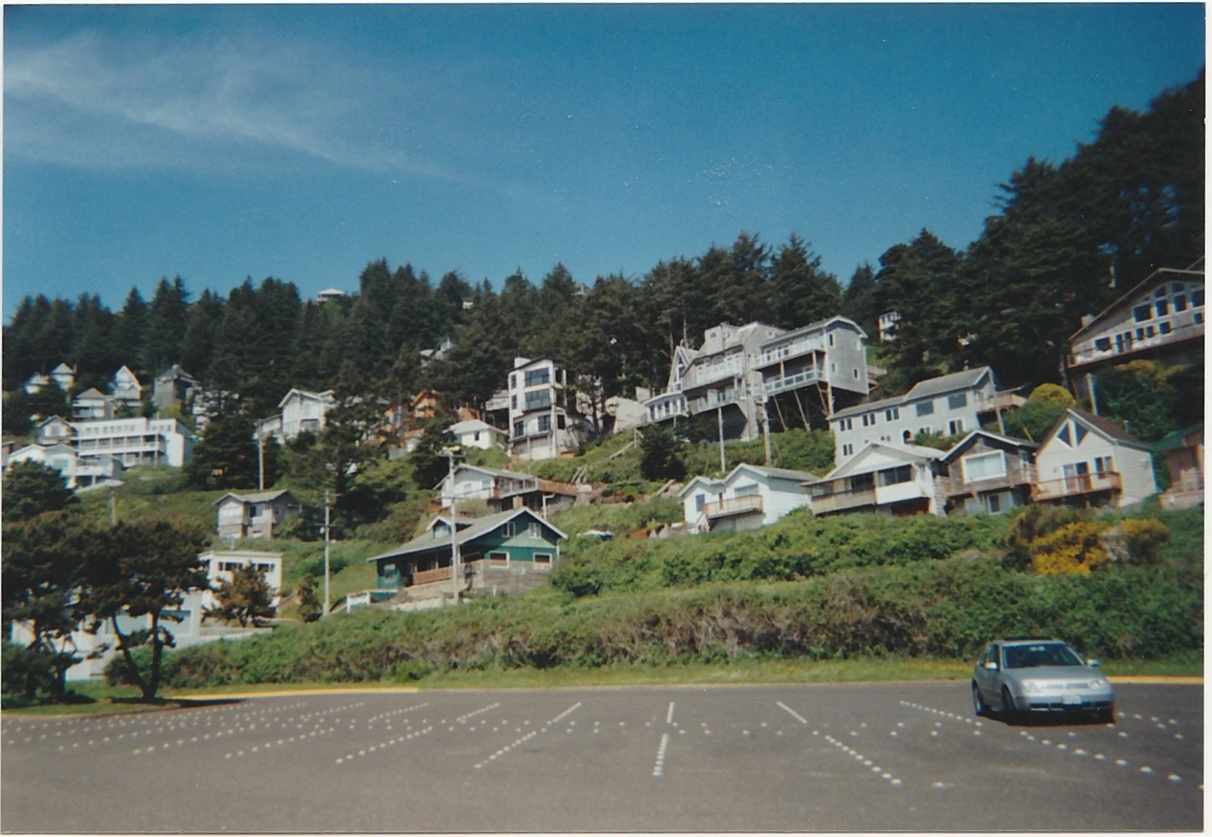 Hillside neighborhood overlooking a parking area, with houses nestled among evergreen trees.