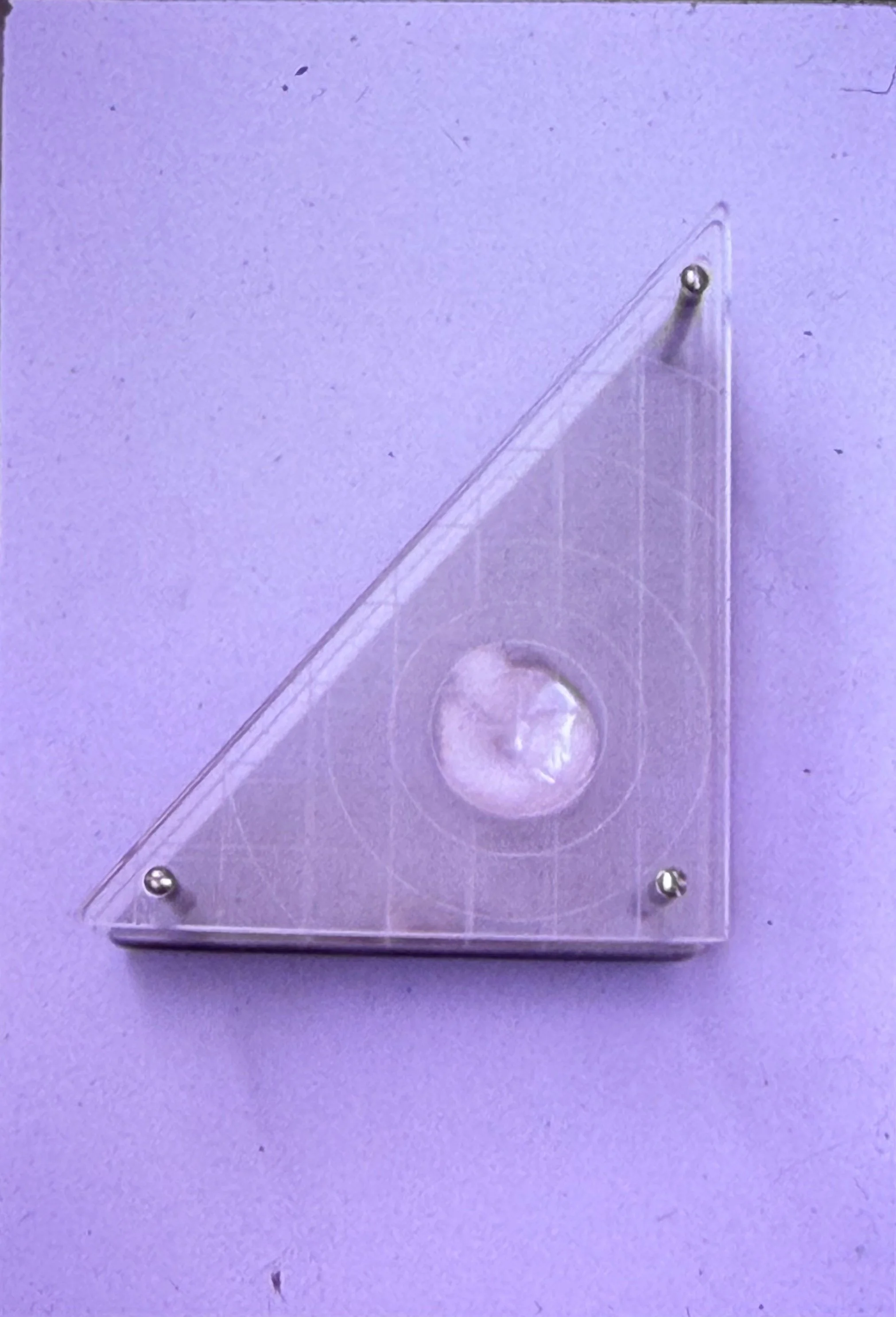 Triangular transparent sculpture containing a suspended circular element within a clear acrylic frame.