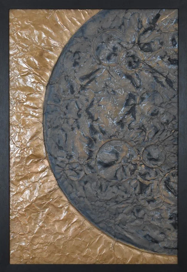A cratered dark world curves across a luminous golden field. Shown close up in a black frame.