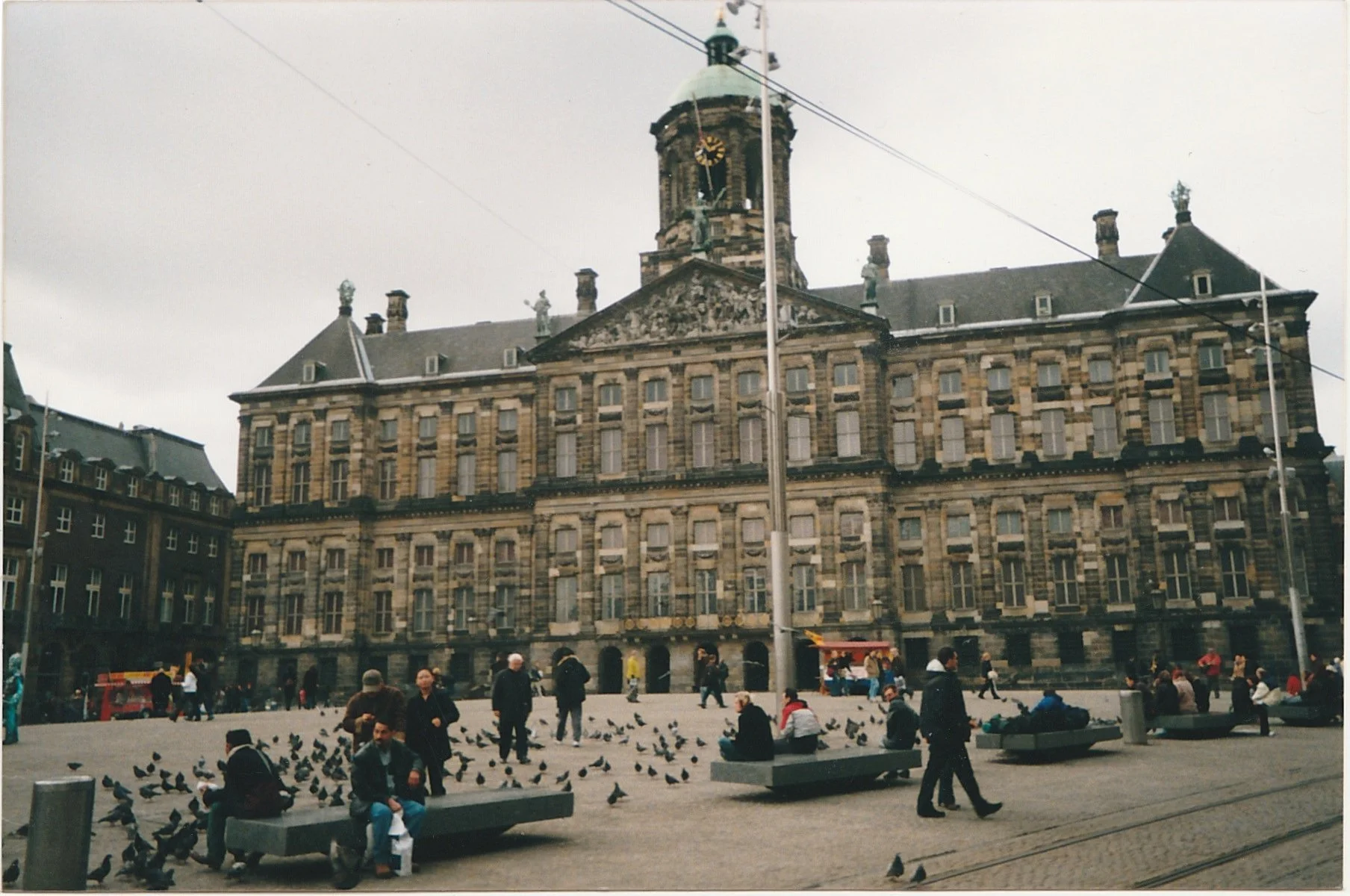 Historic city square filled with people and pigeons gathered before a grand civic building.