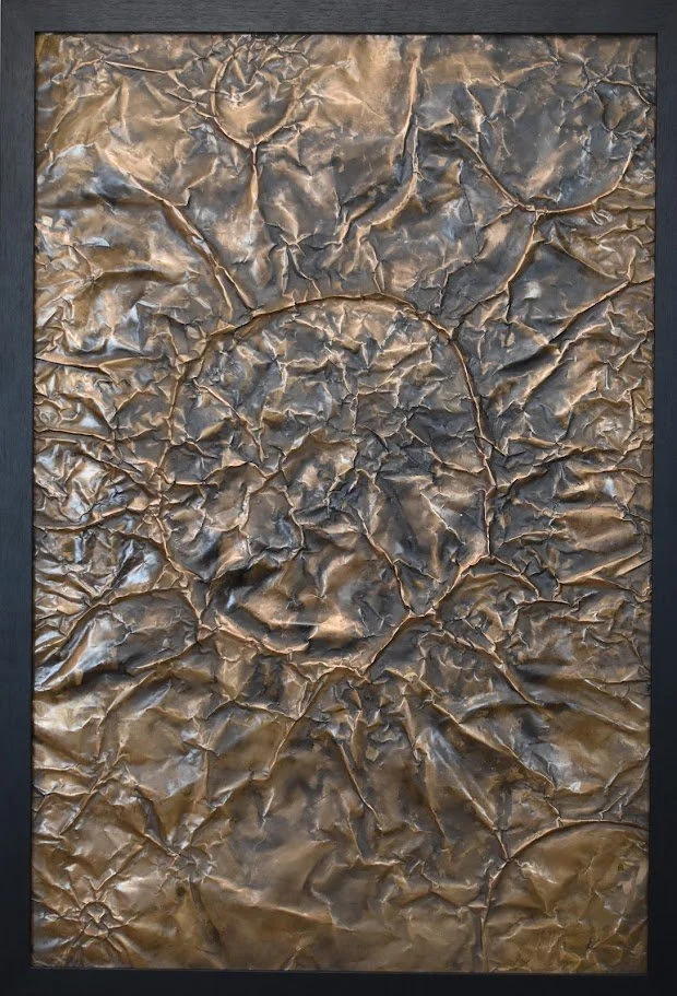 A fractured metallic surface in shifting bronze and charcoal tones. Shown close up in a black frame.