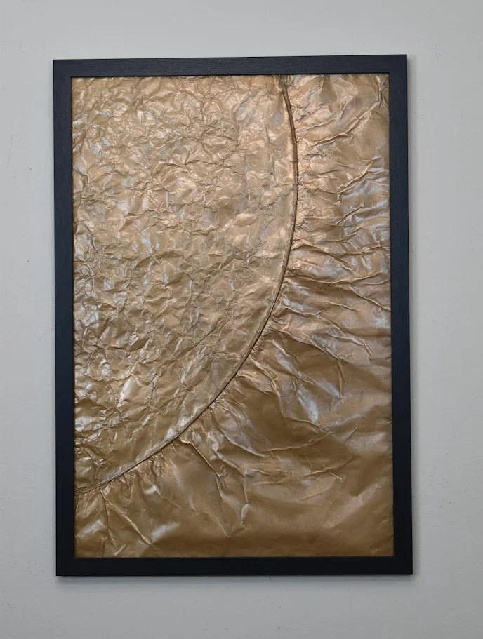 A sweeping golden arc divides contrasting metallic textures. Displayed framed on a white wall.