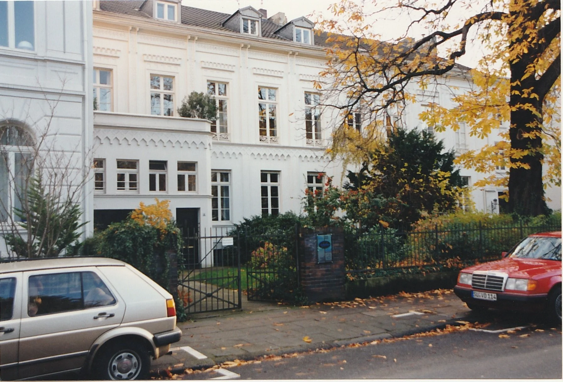 Residential street lined with large historic homes and autumn trees.