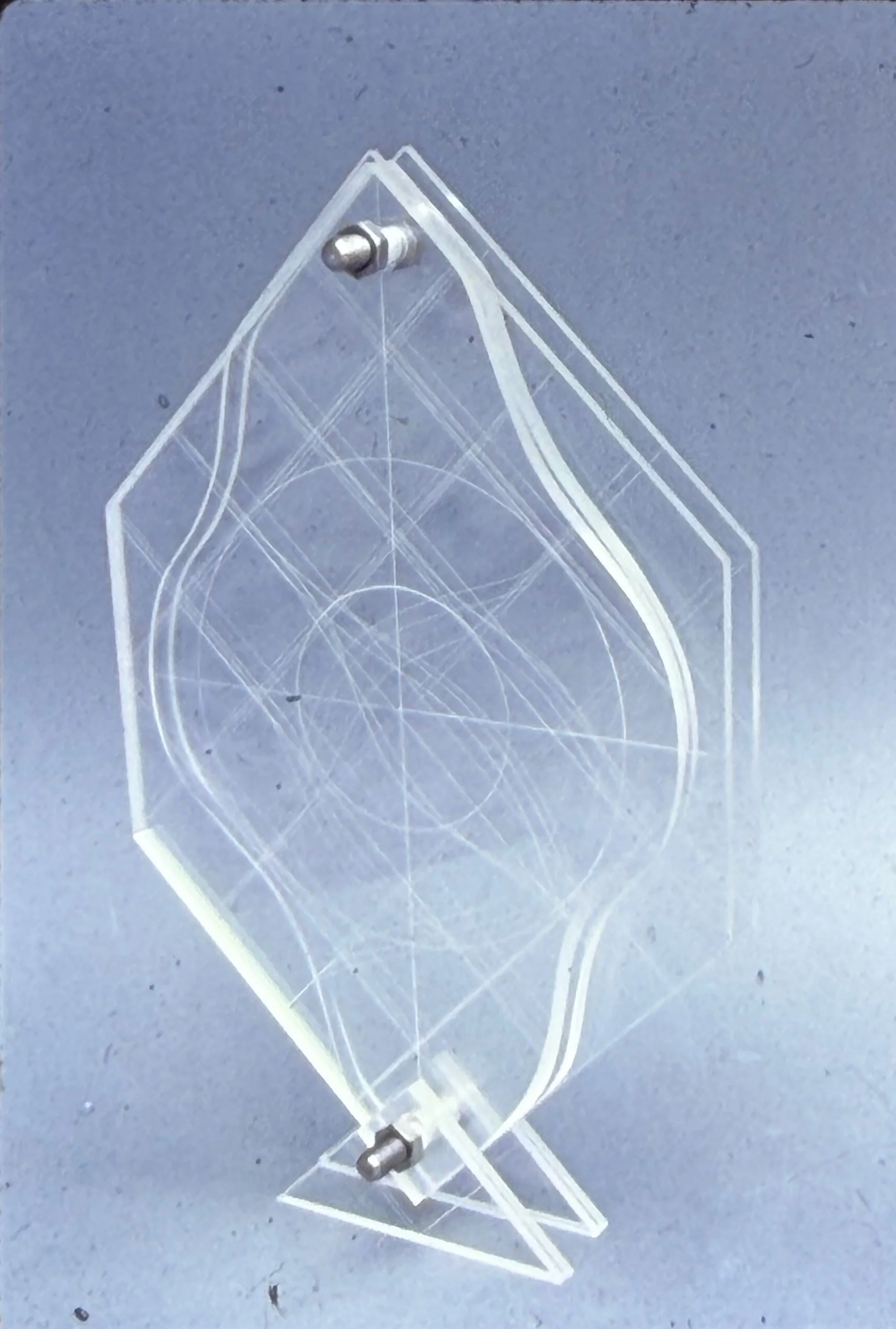 Abstract acrylic sculpture formed from overlapping transparent geometric shapes etched with curved line patterns.