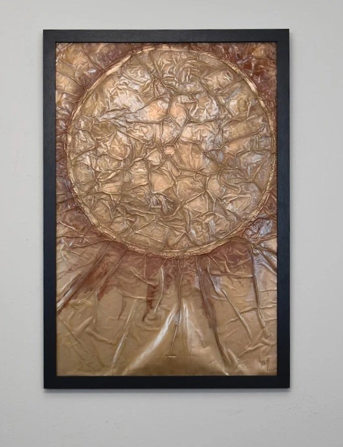 A luminous golden orb emerges from flowing metallic textures. Displayed framed on a white wall.