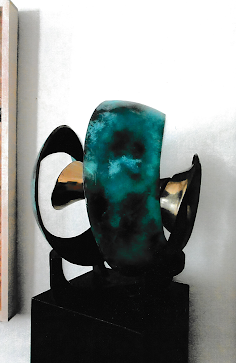 Abstract sculpture composed of large turquoise and black curved forms arranged in concentric loops around a central opening.