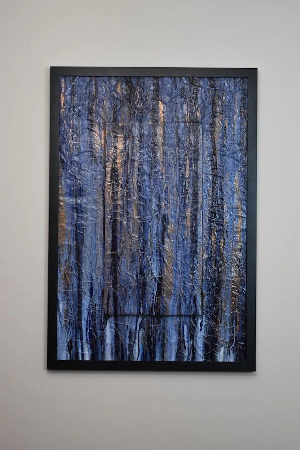 Vertical blue and black currents flow across a textured metallic field. Displayed framed on a white wall.