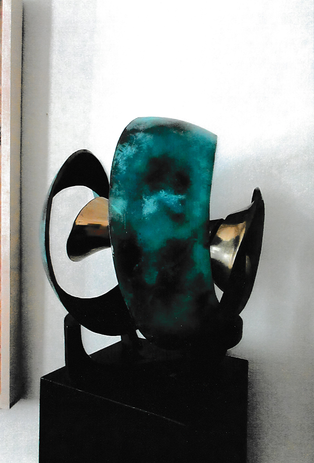 Abstract sculpture combining broad turquoise surfaces with black circular elements and sweeping curved shapes arranged around a central void.