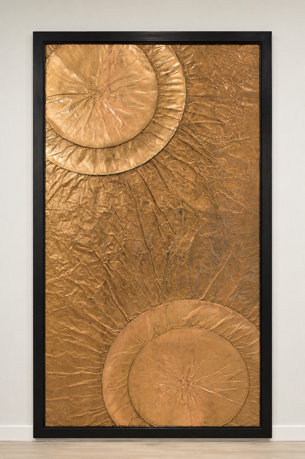 Large overlapping circular forms emerge from opposite corners of a warm metallic field. Displayed framed on a white wall.