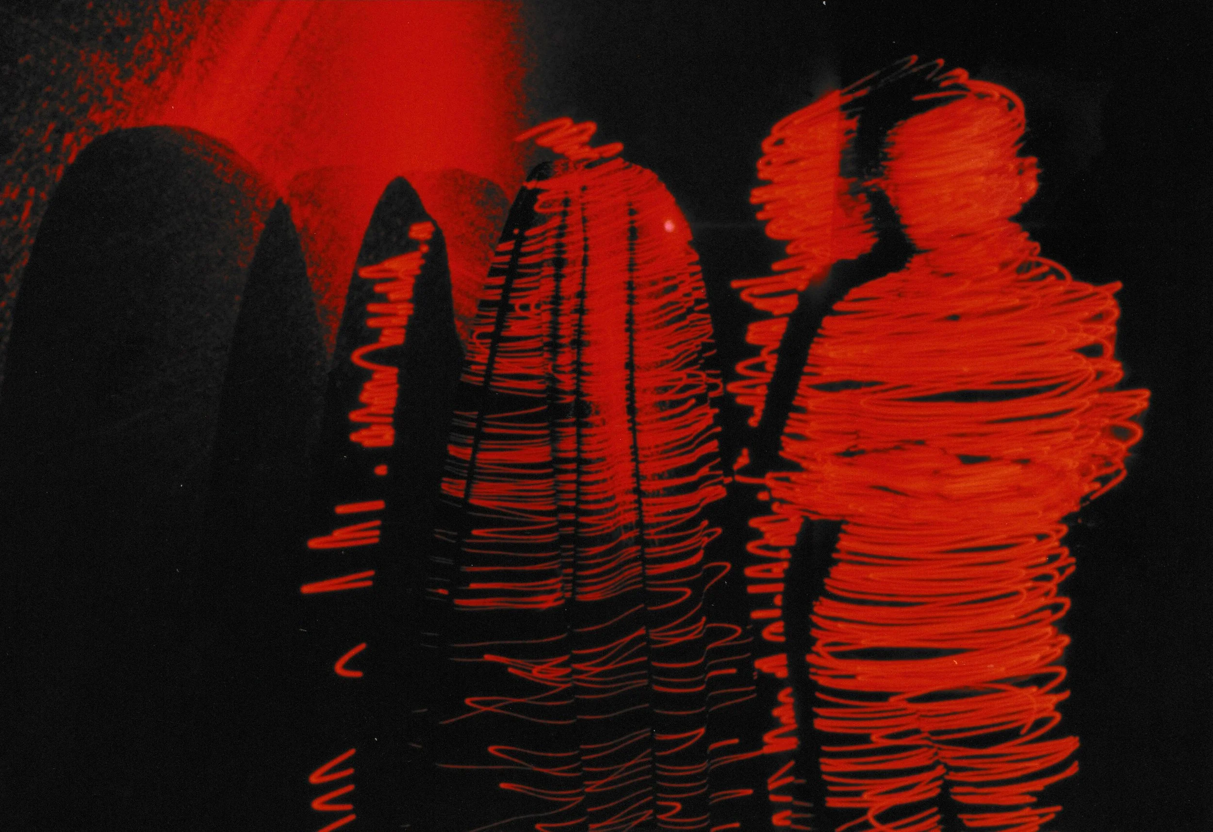 Red laser light radiating from a sculptural form atop a pedestal, producing swirling lines and glowing patterns throughout the composition.