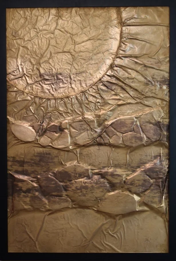 A golden orb rises above layered, fractured metallic forms. Shown close up in a black frame.