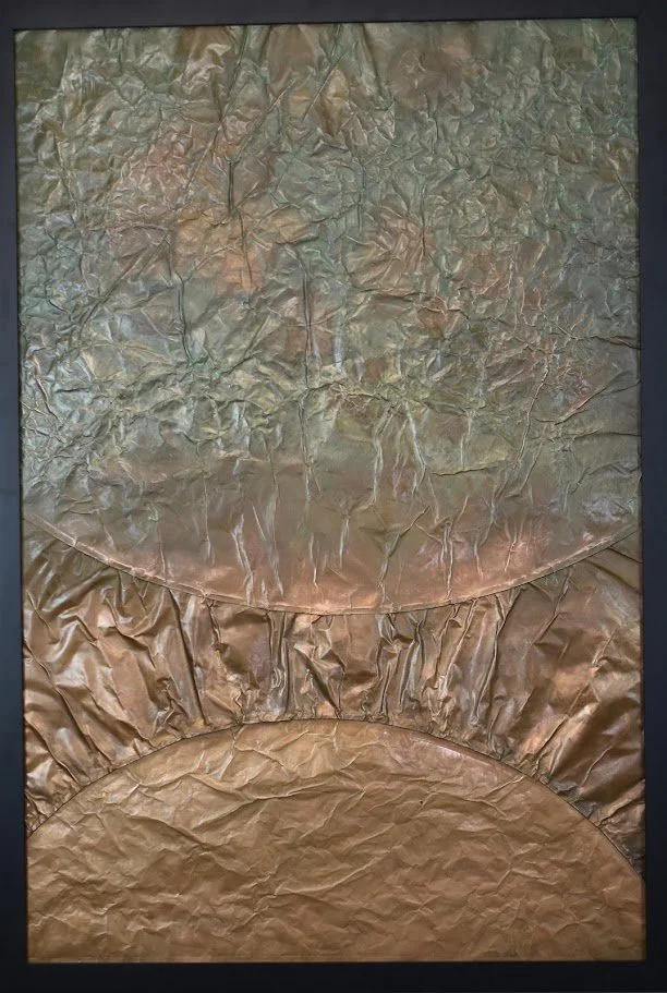 Layered metallic arcs rise through a muted silver and copper field. Shown close up in a black frame.