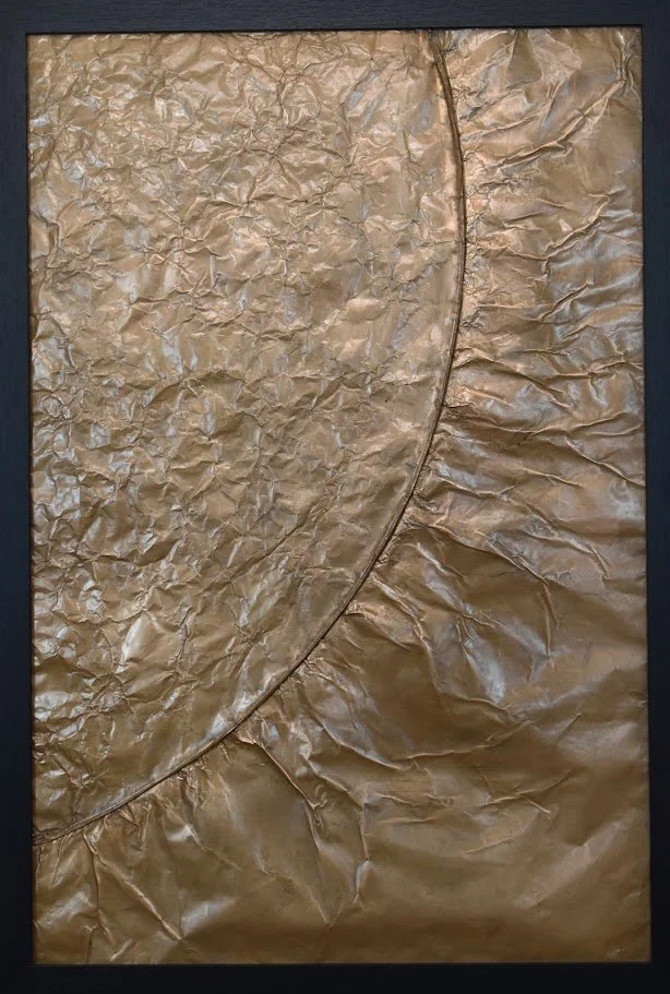 A sweeping golden arc divides contrasting metallic textures. Shown close up in a black frame.