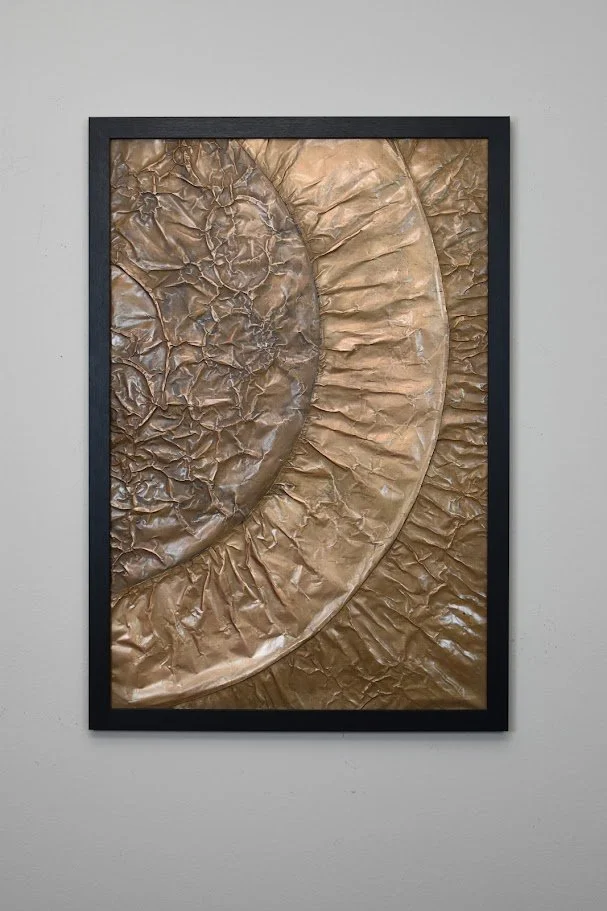 Concentric golden arcs radiate across a textured metallic field. Displayed framed on a white wall.