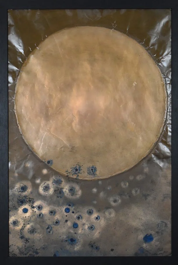 A textured metallic composition dominated by a large golden orb above a field of scattered blue and silver circular forms. Shown close up in a black frame.