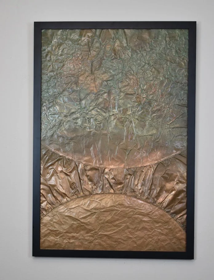 Layered metallic arcs rise through a muted silver and copper field. Displayed framed on a white wall.