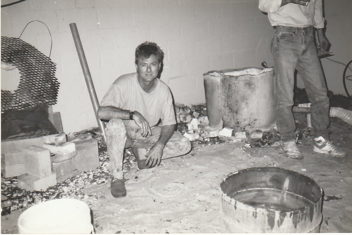 Whitney Wolf at work in a bronze foundry, surrounded by casting equipment, molds, and materials used in the bronze-making process. Circa 1980s