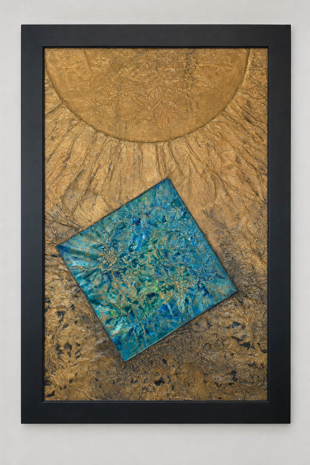 A textured metallic composition featuring a large golden celestial form radiating above a tilted blue square. Displayed framed on a white wall.