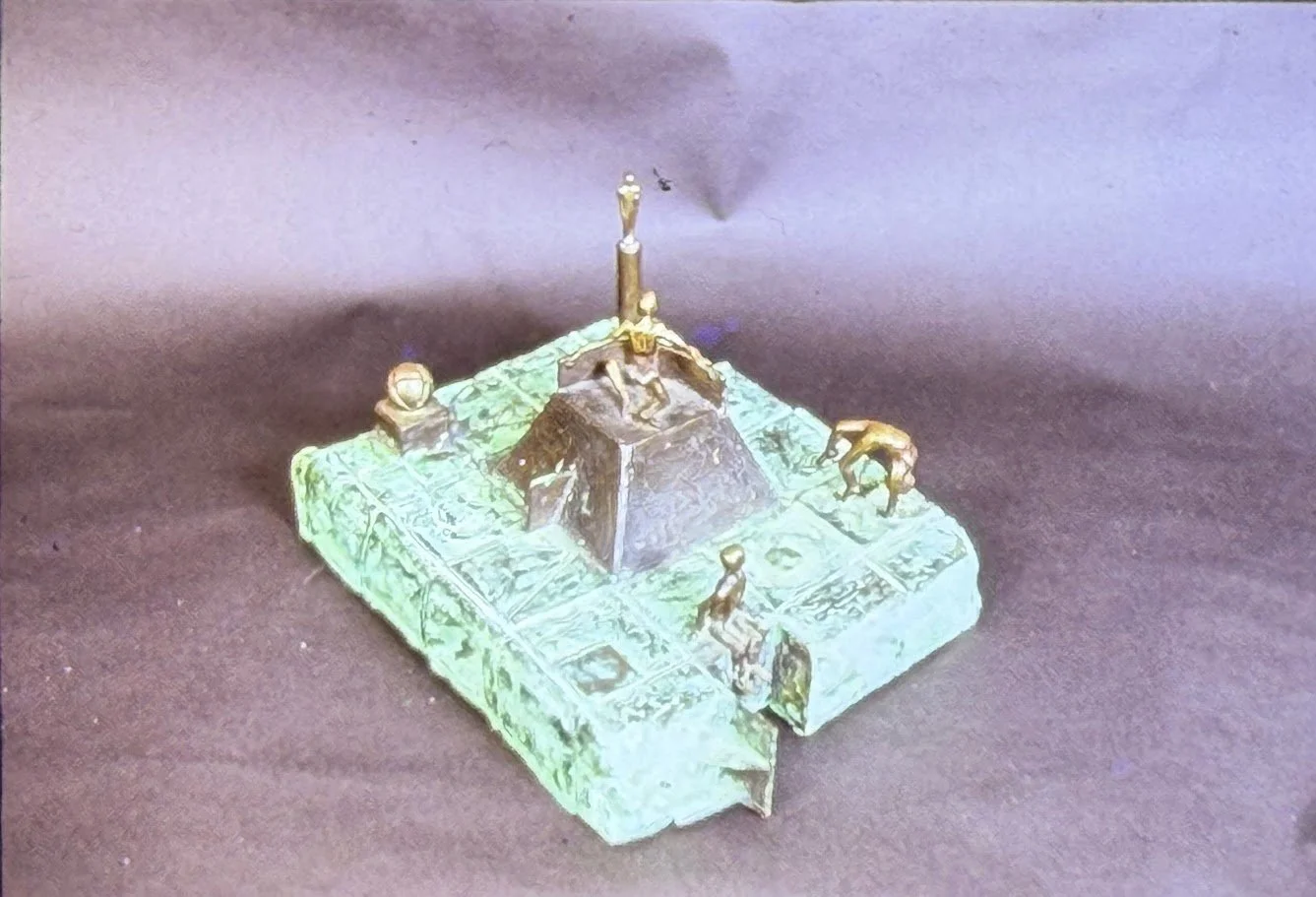 Miniature bronze landscape featuring figures positioned around a central mound or monument. Textured surfaces and geometric details suggest pathways and architectural ruins.