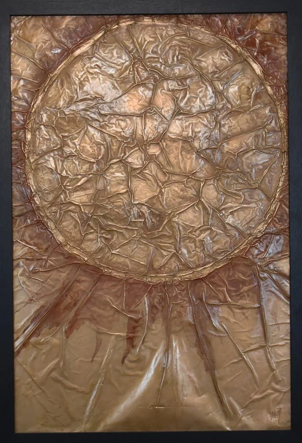 A luminous golden orb emerges from flowing metallic textures. Shown close up in a black frame.