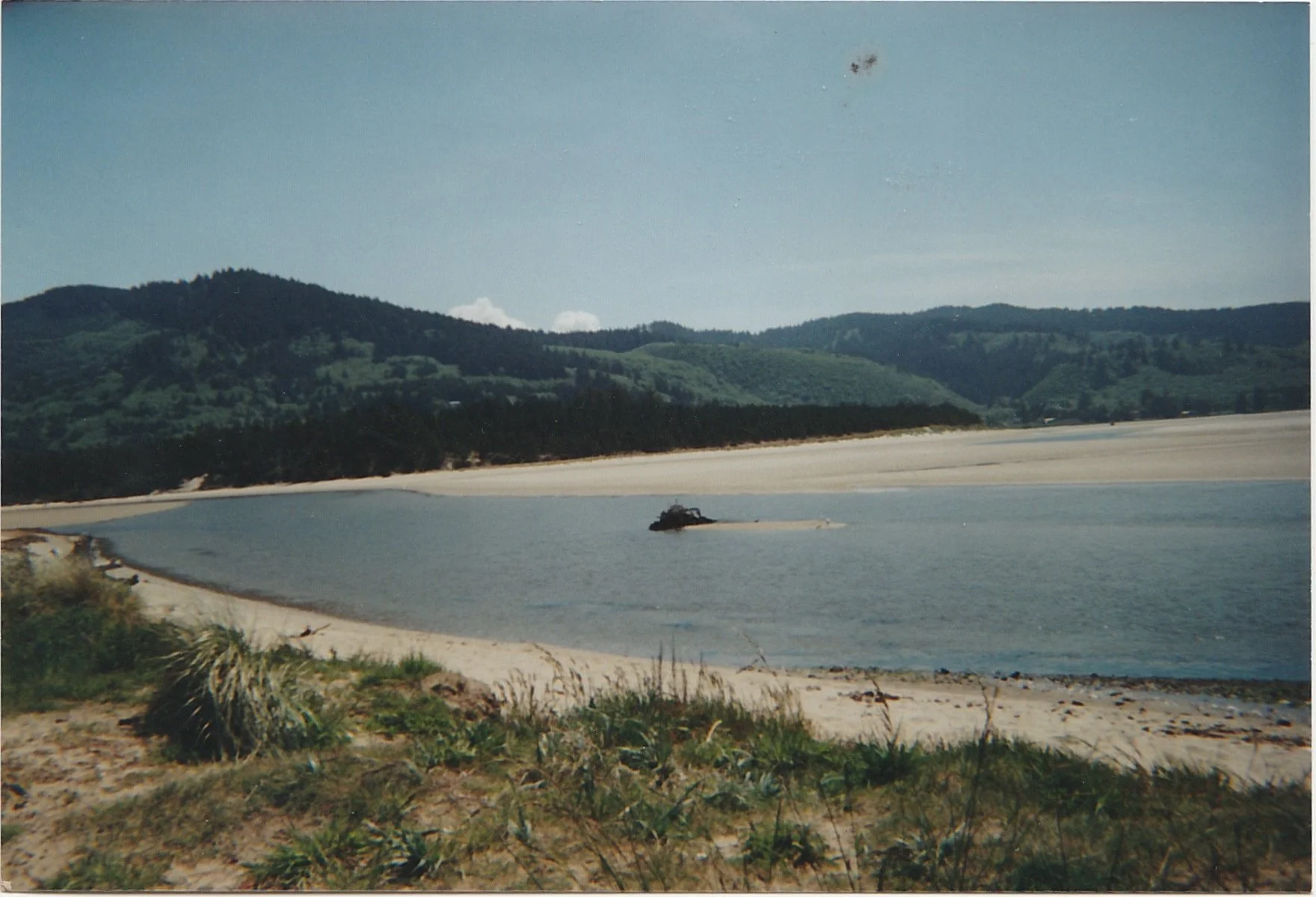 Broad coastal bay framed by rolling green hills and sandy shoreline.