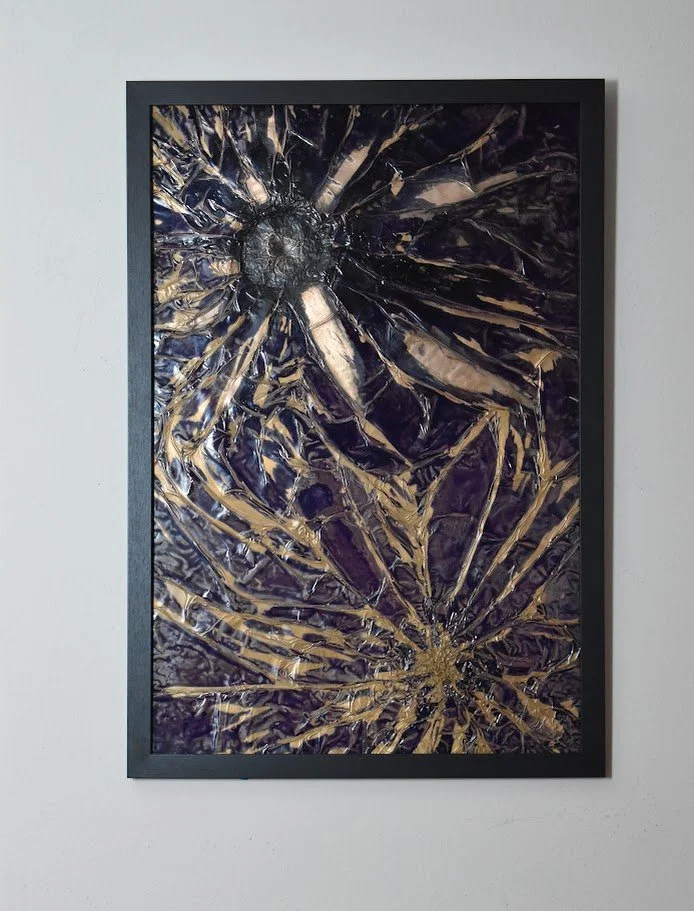 Radiating gold forms burst across a deep violet field. Displayed framed on a white wall.