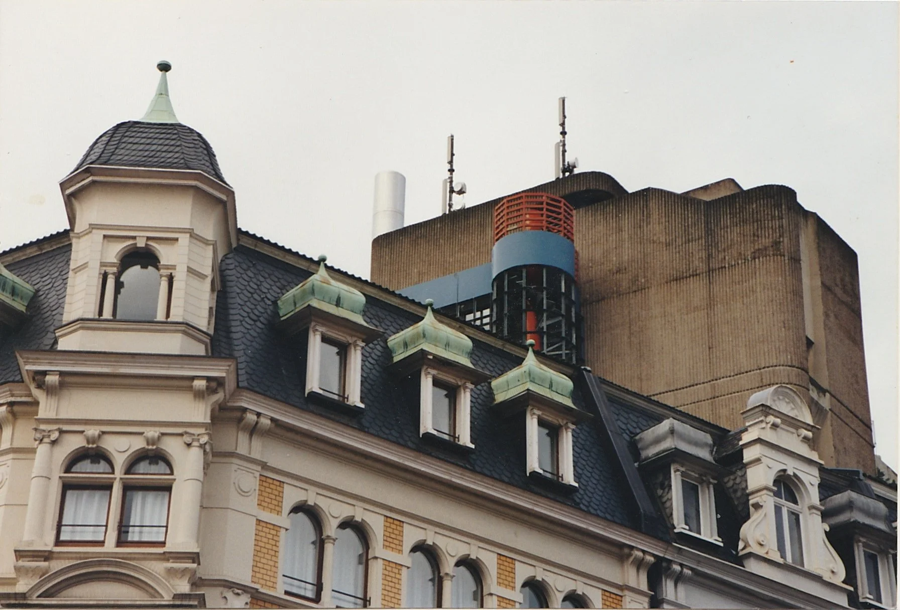 Historic European building combining ornate nineteenth-century architecture with modern structures behind it.