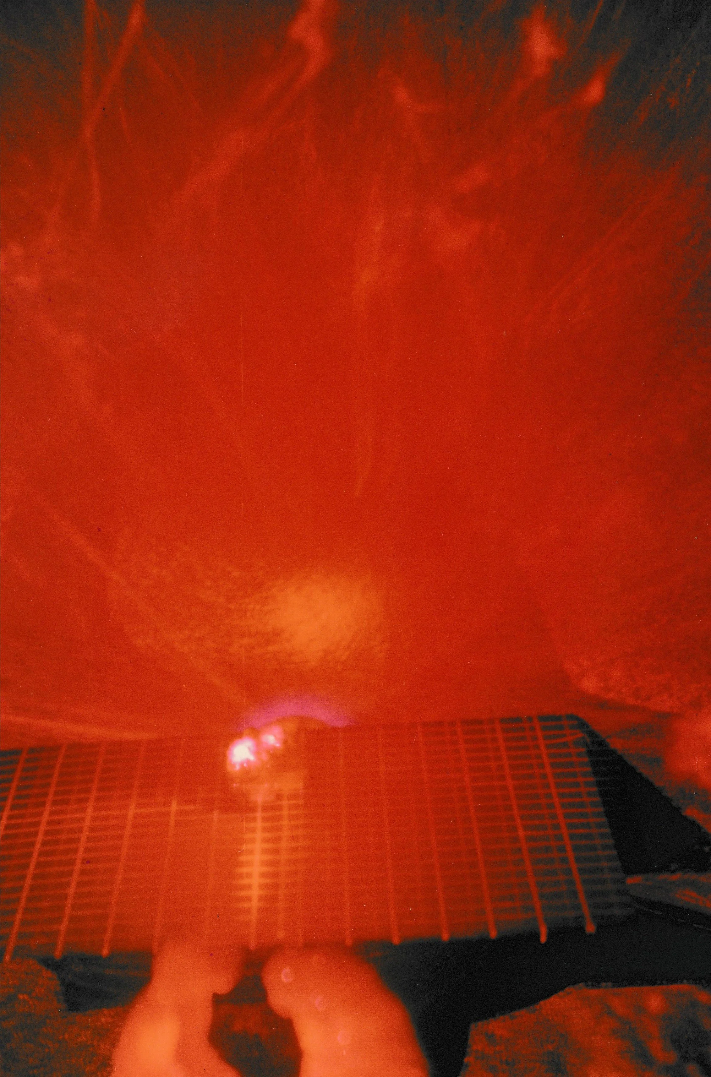 Laser-lit installation with red light radiating across a gridded surface and surrounding sculptural elements.